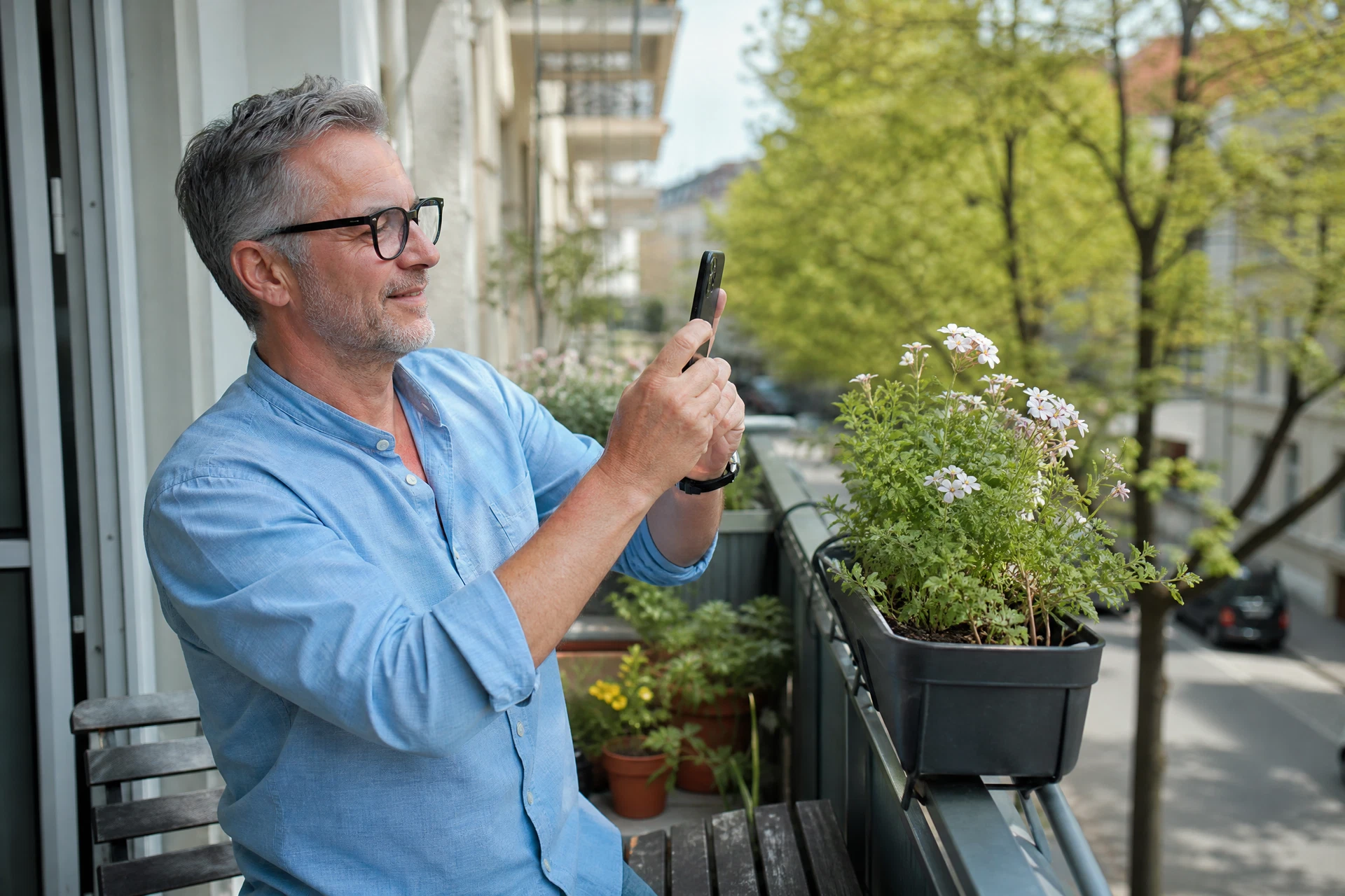 Mann fotografiert eine Pflanze auf dem Balkon mit seinem Smartphone
