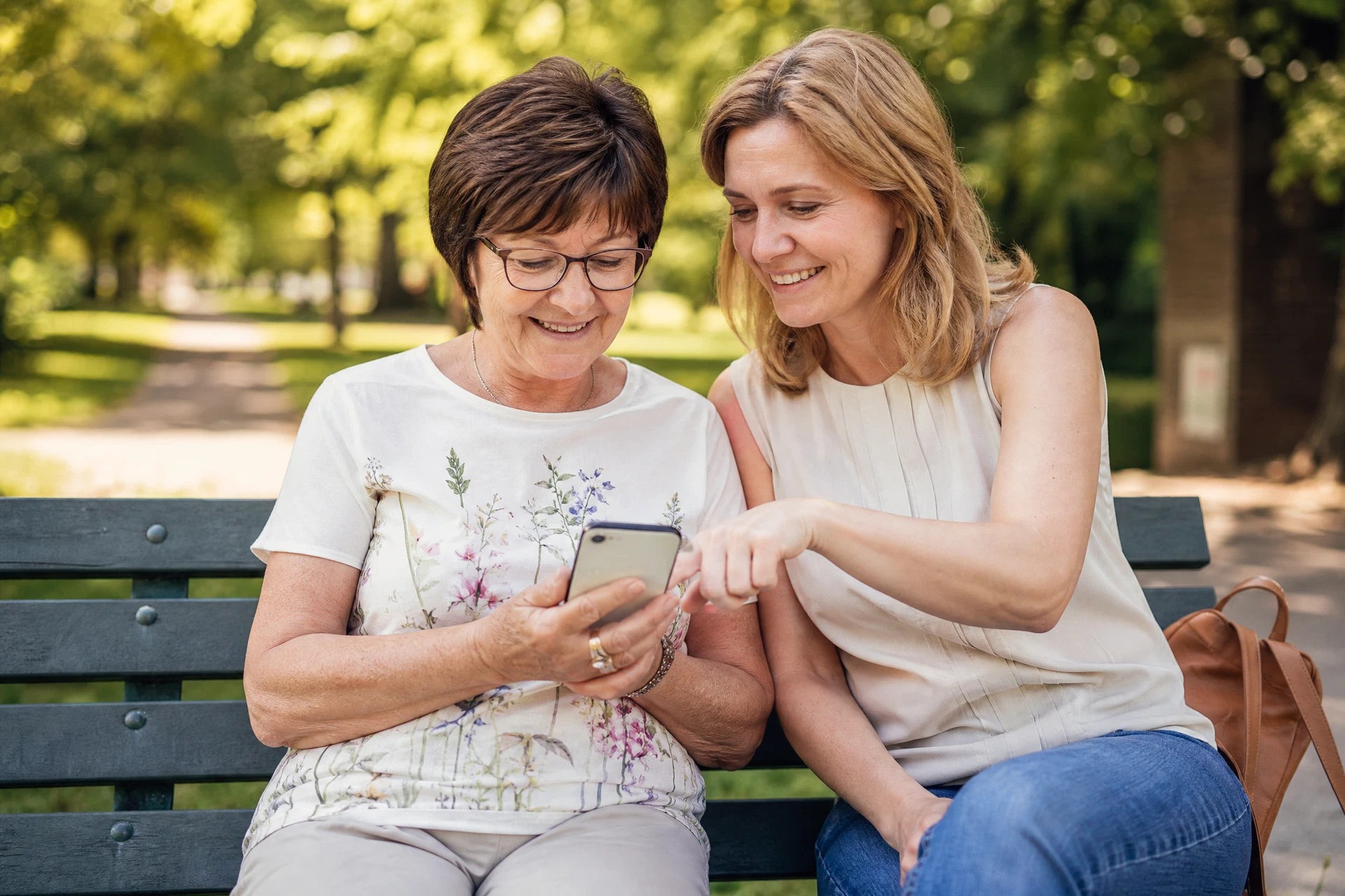 Großmutter und Tochter üben gemeinsam Smartphone-Funktionen auf einer Parkbank